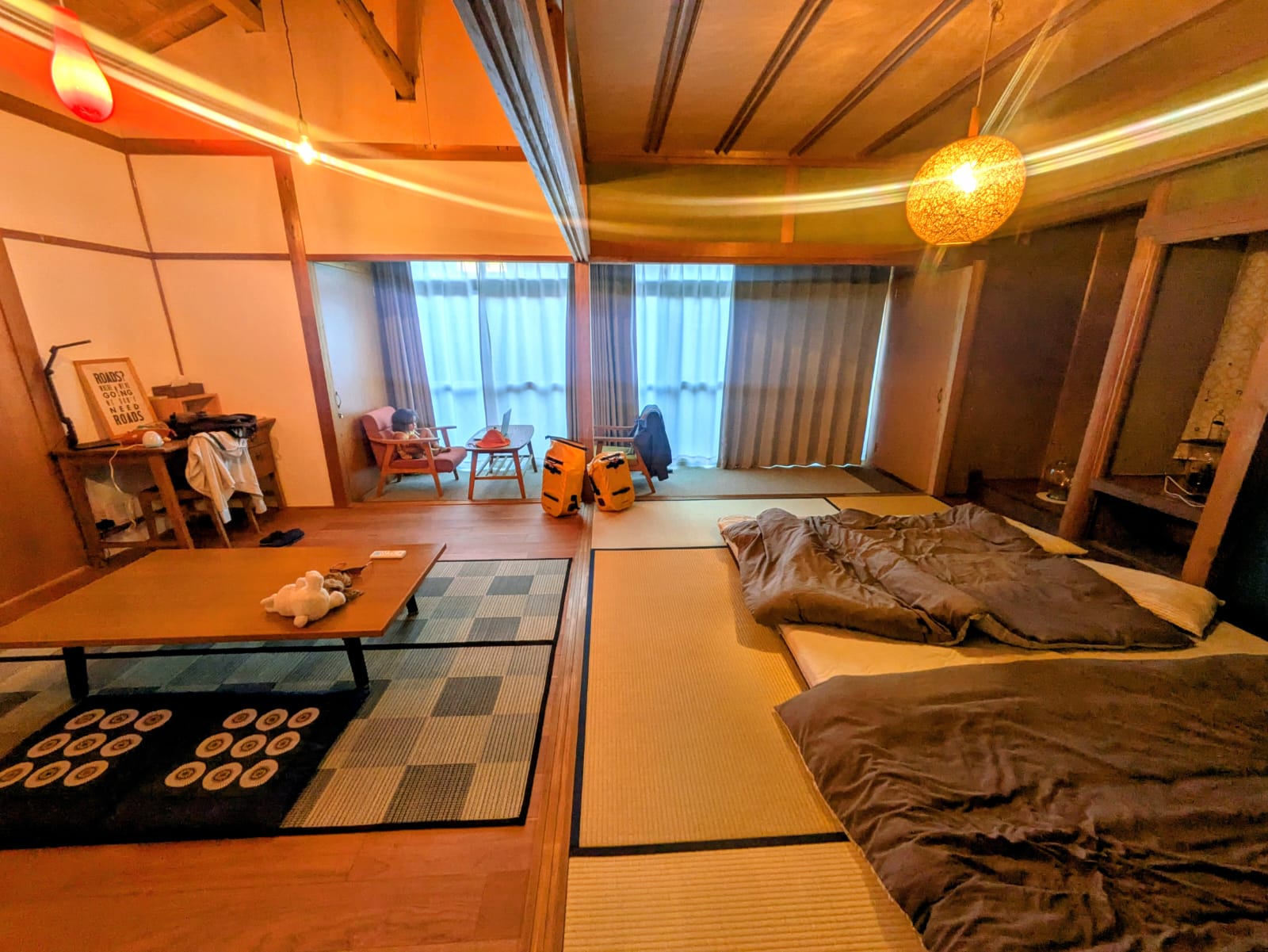 Intérieur d'un ryokan japonais, montrant un espace de vie avec tatamis, des fauteuils, une table basse, et des futons disposés sur le sol.