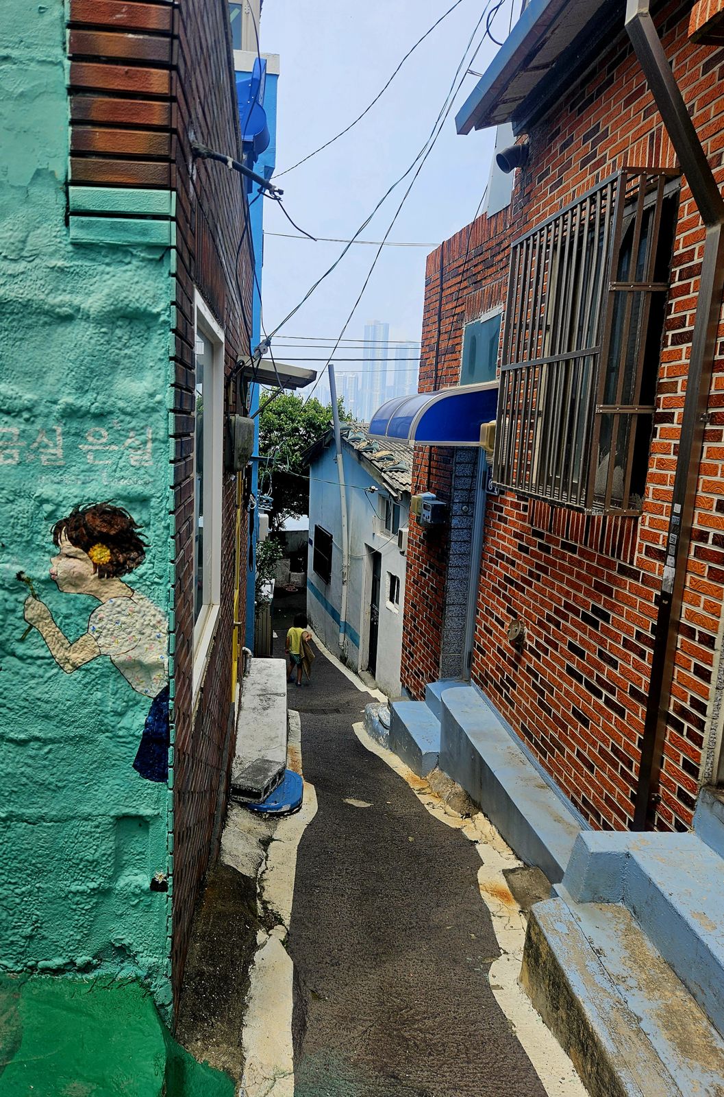 Une ruelle pittoresque à Huinnyeoul avec des maisons colorées, une fresque murale représentant une petite fille et un chemin pavé menant à des bâtiments historiques.