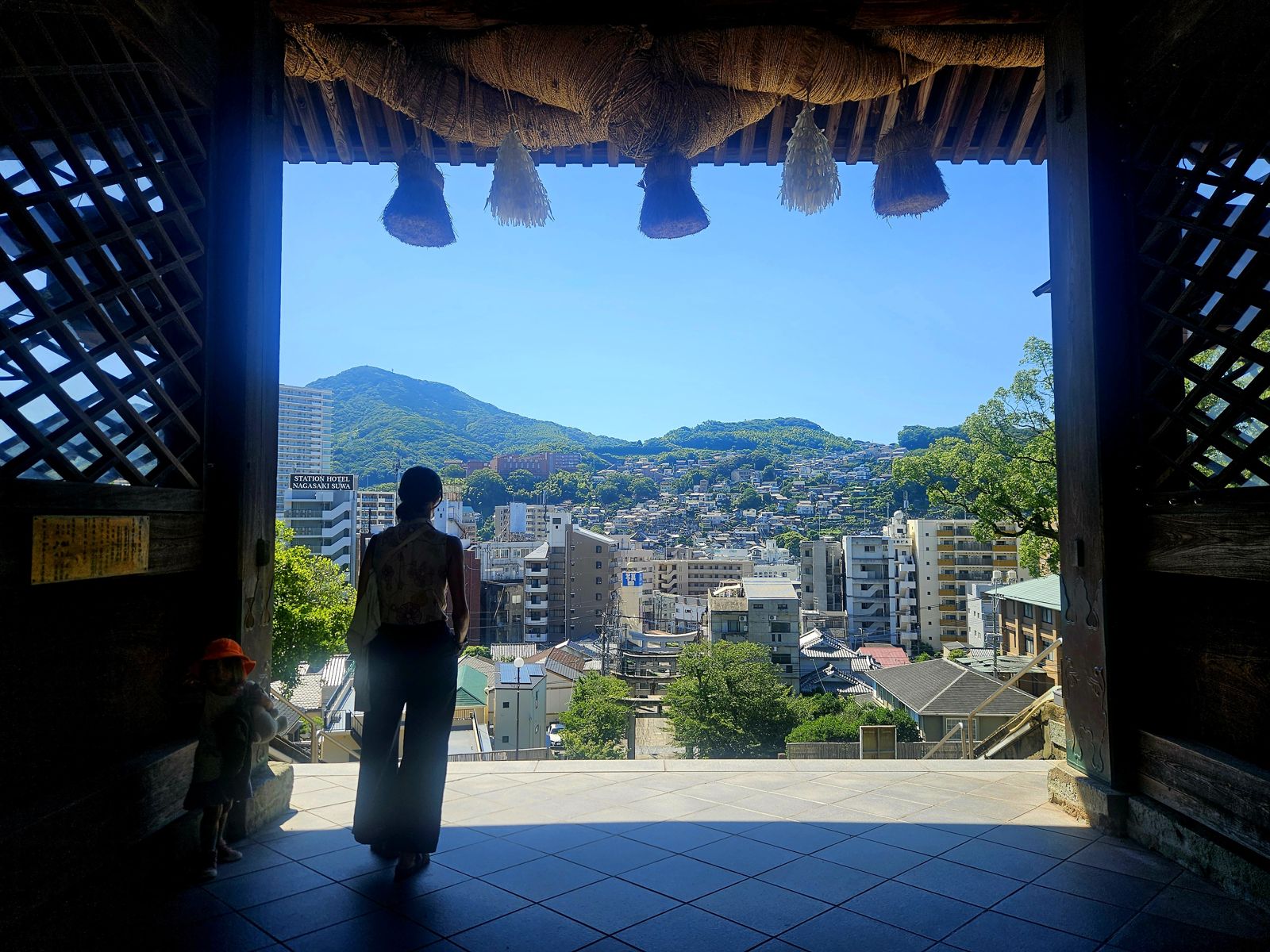Vue depuis un temple avec une silhouette de femme regardant le paysage urbain et les collines de Nagasaki.