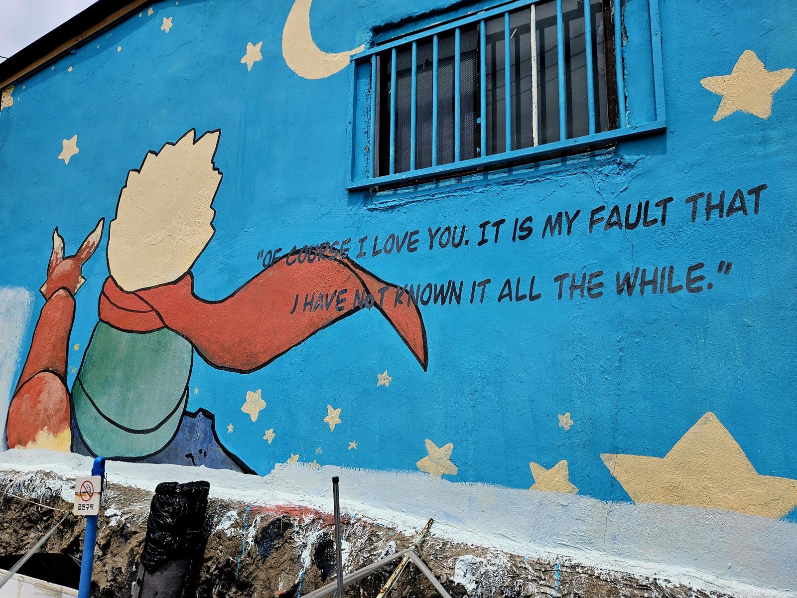 Mur peint représentant le Petit Prince tenant une rose, avec une citation écrite en anglais sur fond bleu, parsemé d'étoiles.