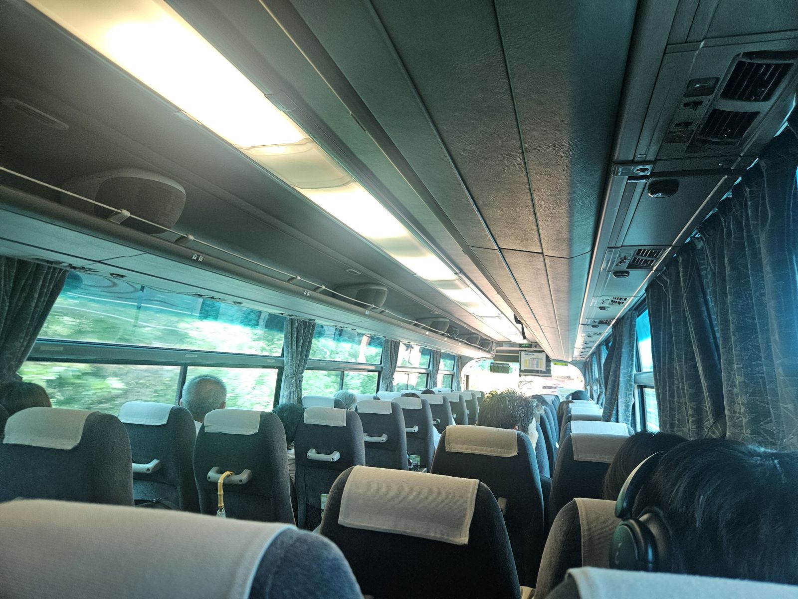 Intérieur d'un bus de campagne, montrant des sièges vides et des passagers assis, avec des fenêtres grandes et des rideaux.