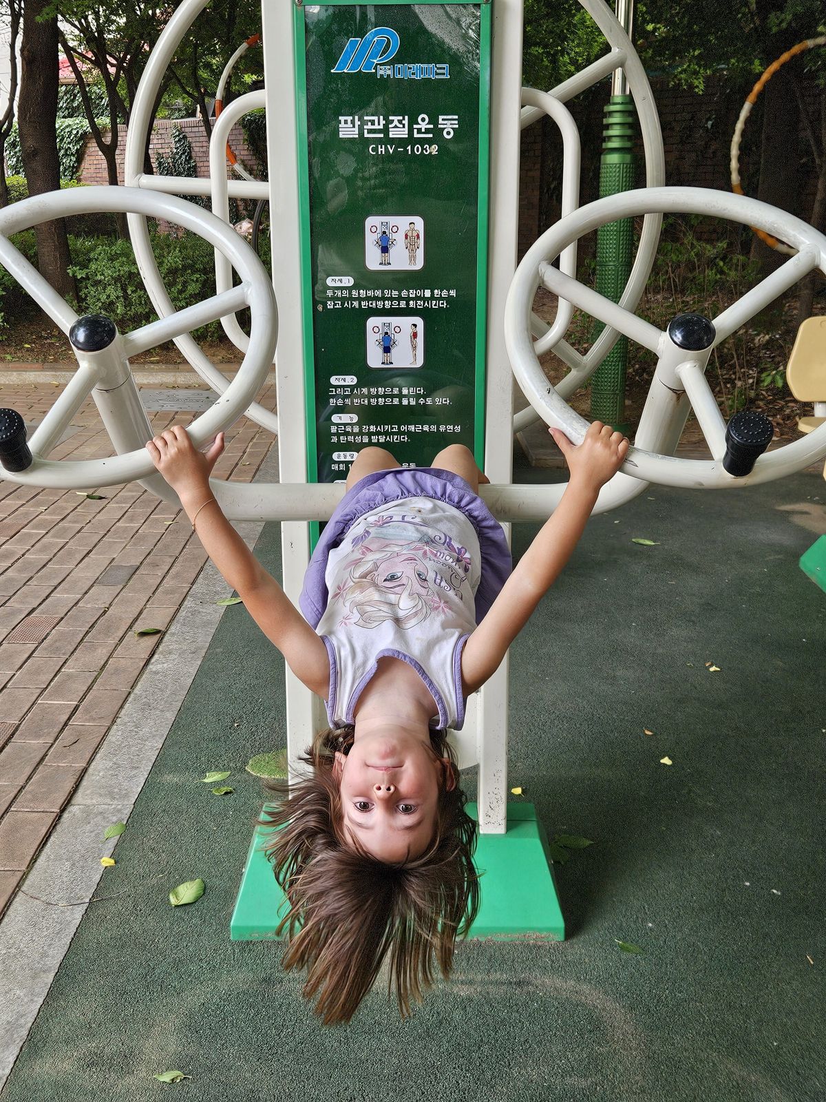 Une enfant s'amuse en faisant de l'exercice sur un appareil de fitness dans un parc, suspendue à l'envers avec les cheveux flottants.