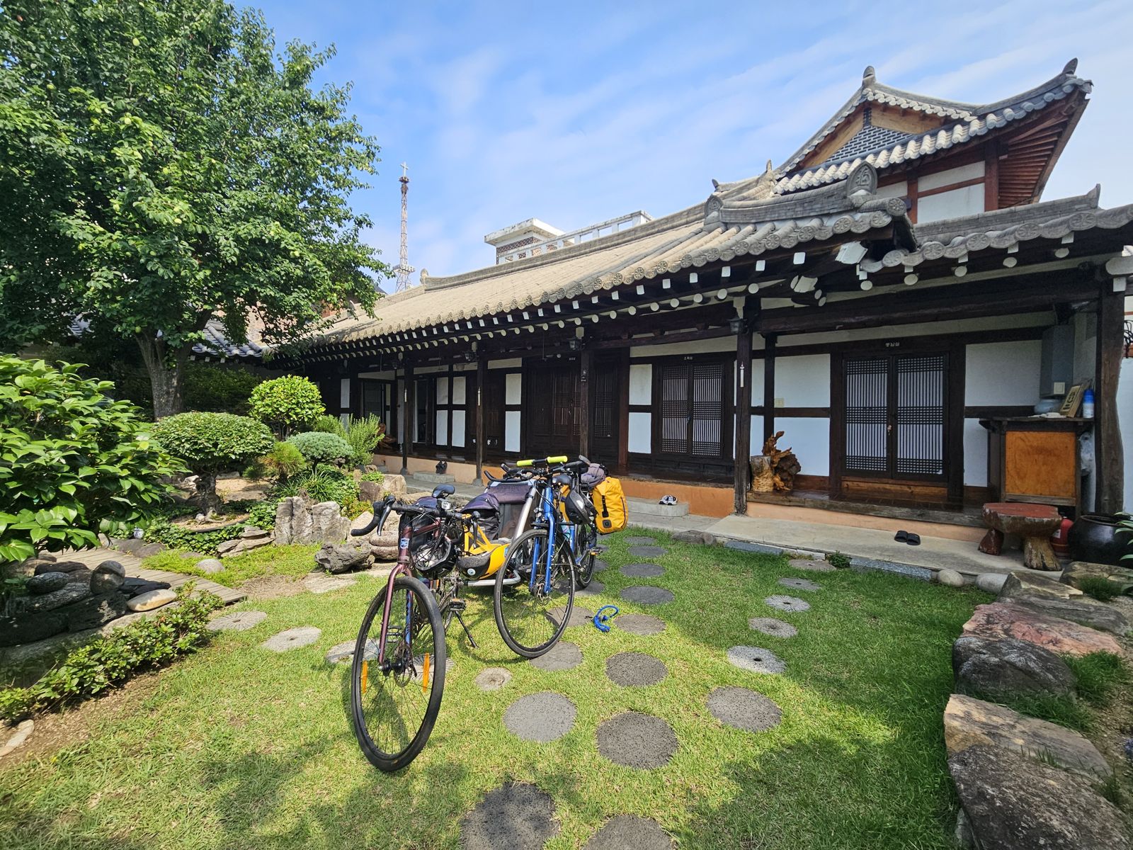 Vue d'une maison traditionnelle coréenne avec jardin, où sont stationnés deux vélos avec des sacs de voyage.