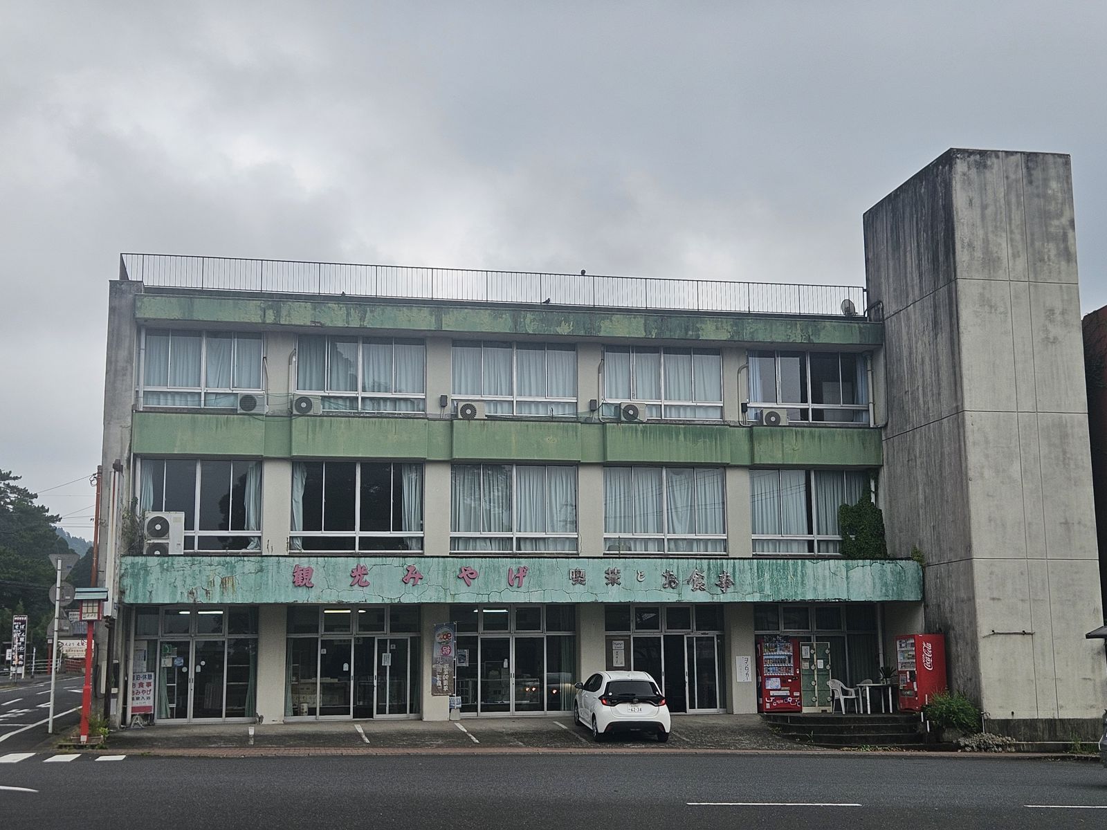 Vue d'un hôtel ancien et décrépit à Kirishima, Japon, avec un extérieur en métal vert et des fenêtres blanches.
