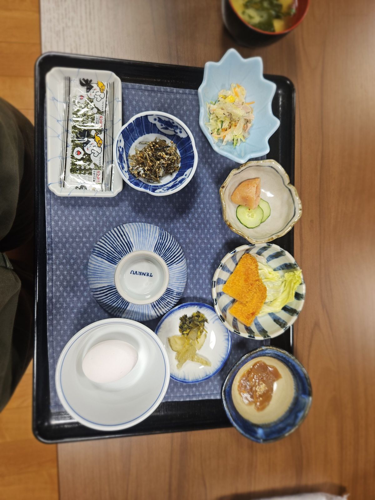 Petit-déjeuner japonais traditionnel comprenant du riz, des légumes, du poisson, des œufs crus et d'autres plats variés, servi sur un plateau en bois.