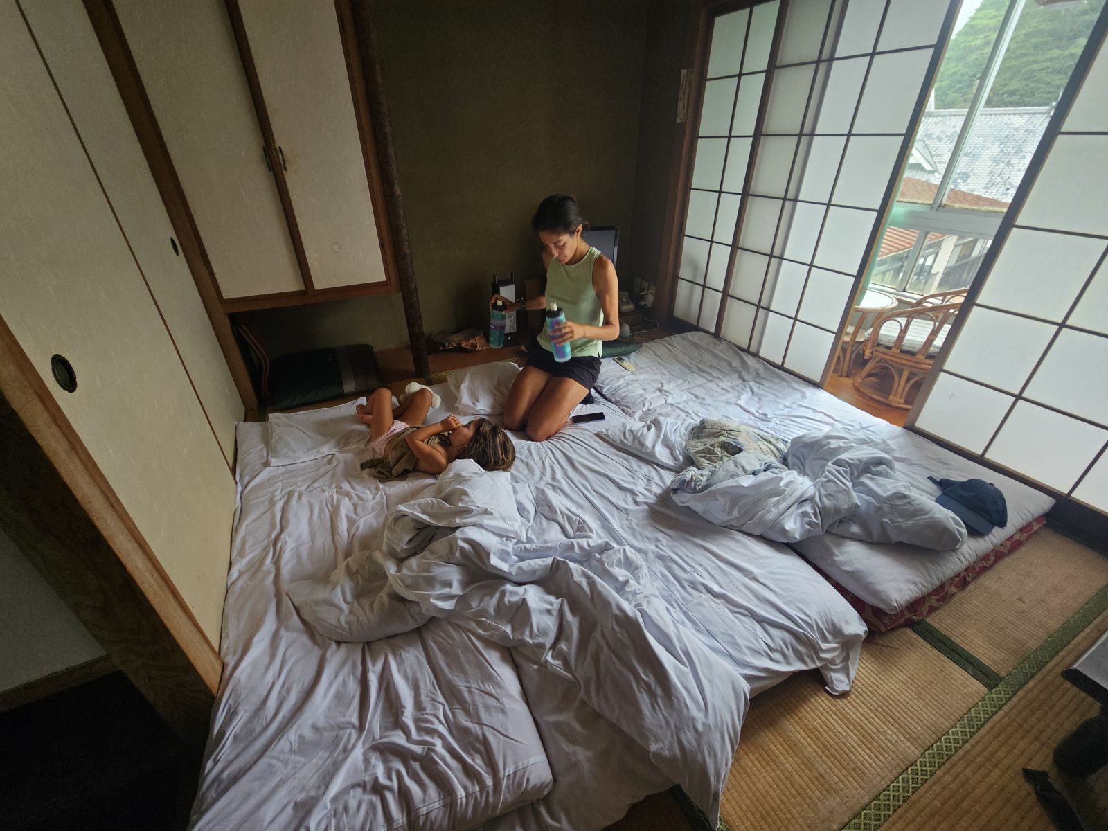 Une mère assise sur un futon avec sa fille dans une chambre à tatami. La pièce a des murs en papier japonais et une vue sur la nature à travers des fenêtres en verre.