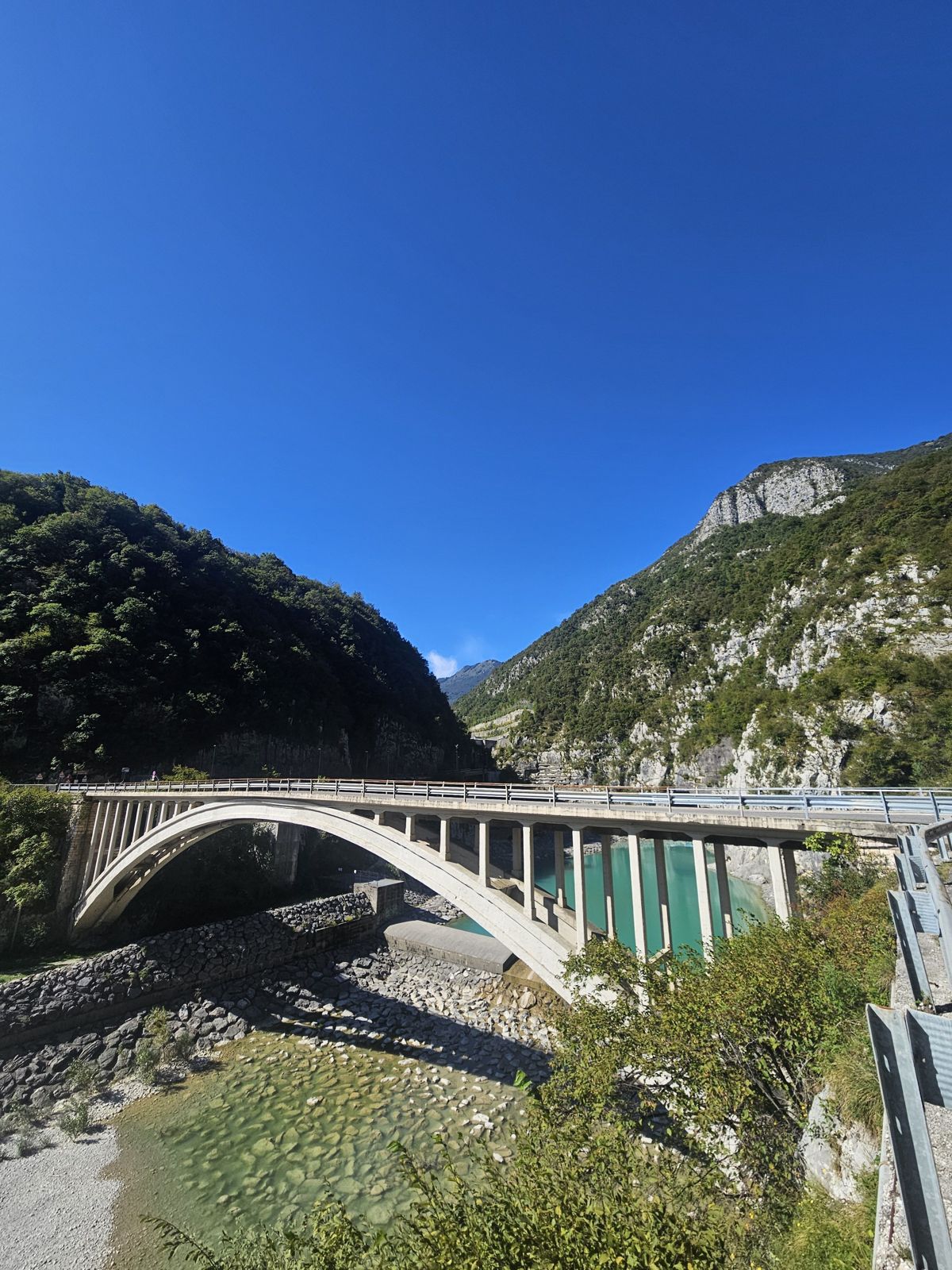 Un pont en béton élégant surplombe une rivière calme, entouré de collines verdoyantes sous un ciel bleu clair.