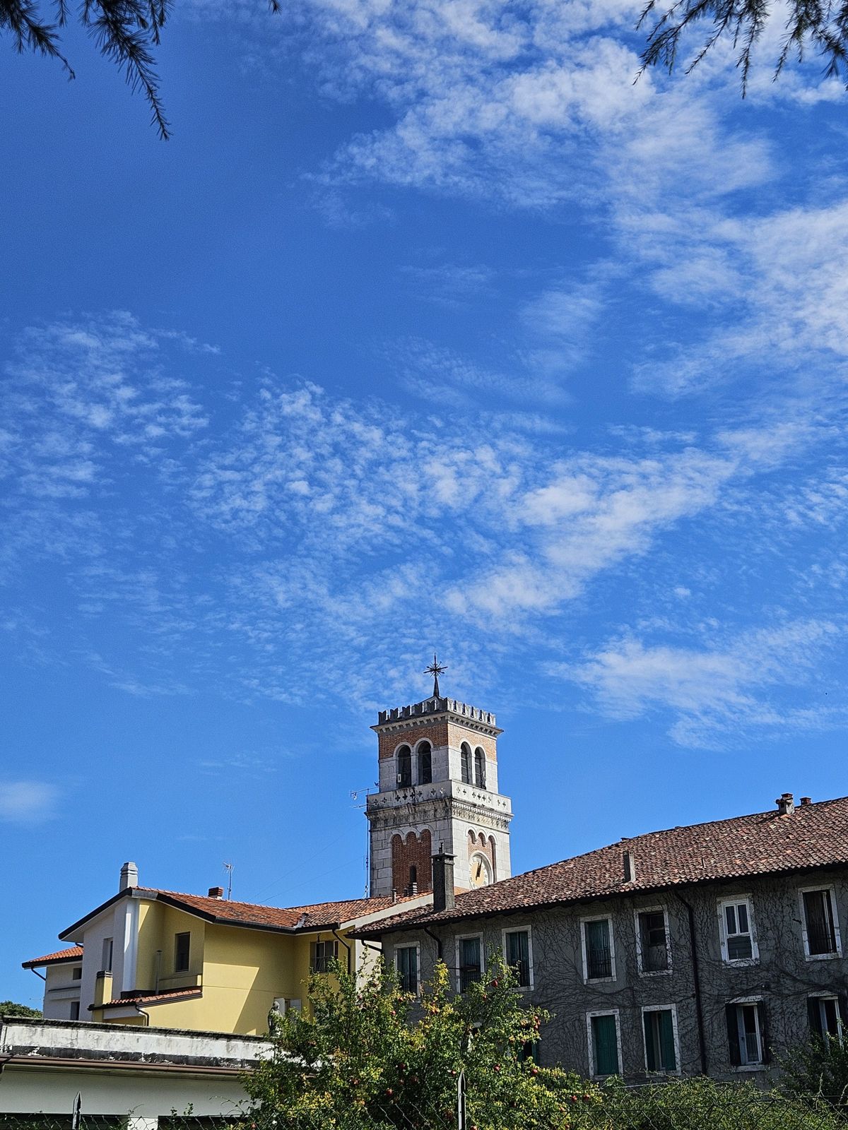 Vue d'une tour d'église sur fond de ciel bleu avec quelques nuages, entourée de bâtiments traditionnels.
