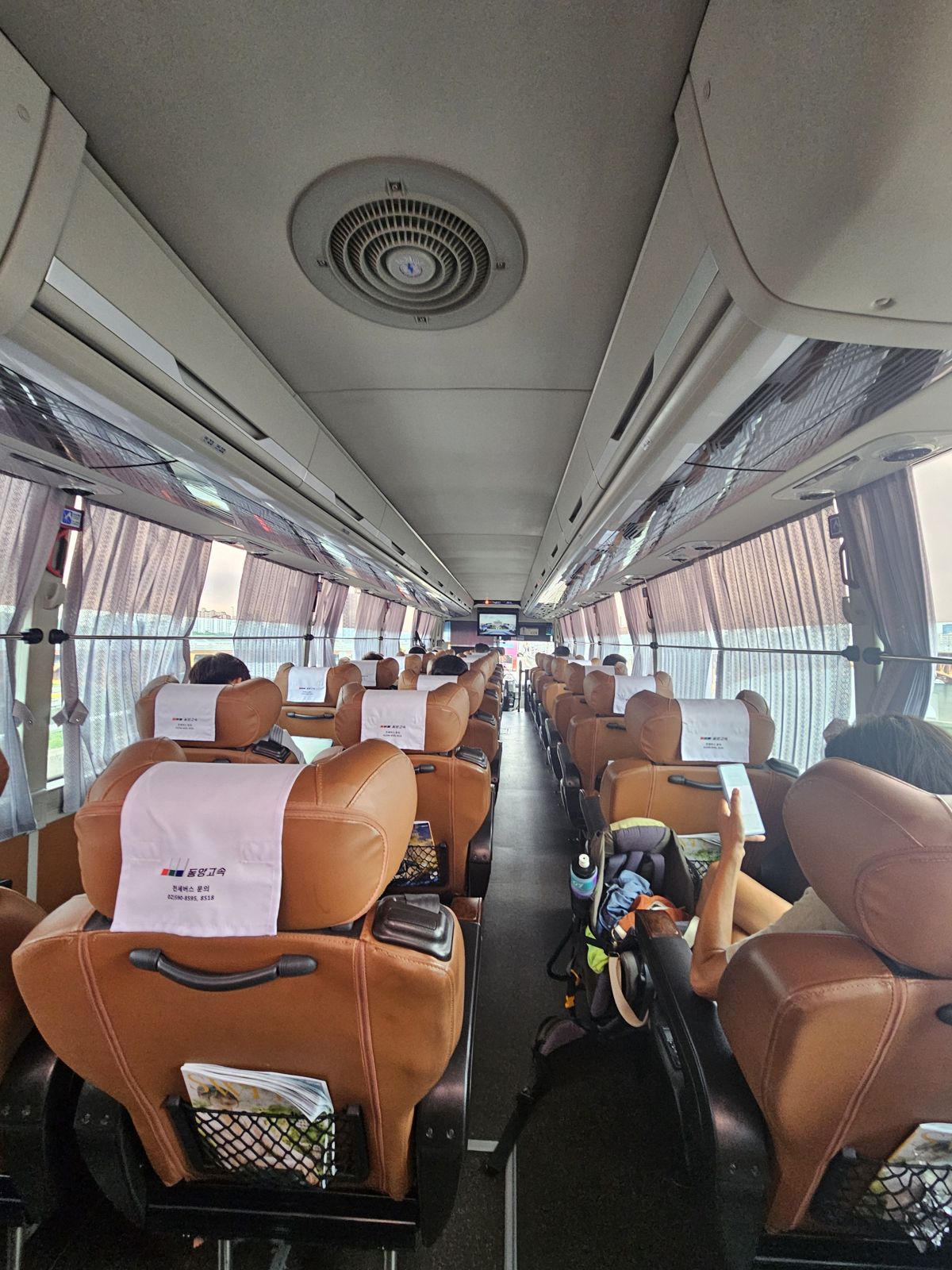 Intérieur d'un bus confortable avec des sièges en cuir marron, panneaux de séparation et rideaux, montrant l'espace et la configuration des places assises.