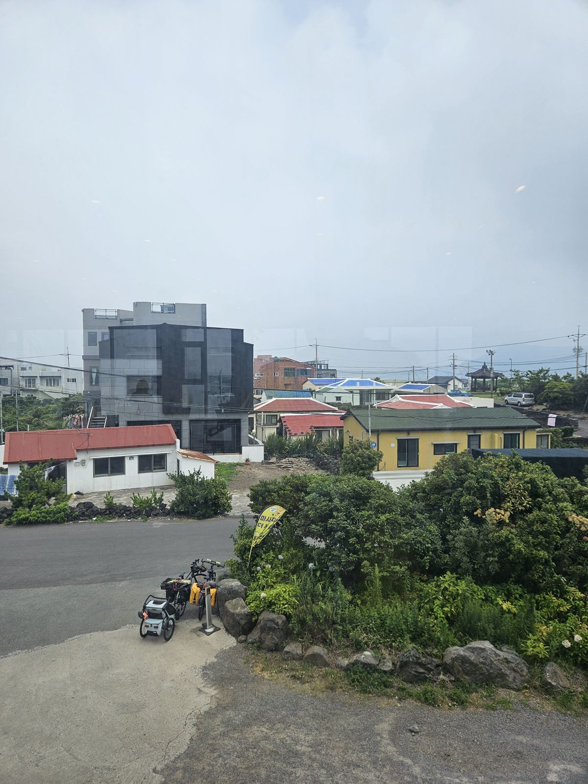 Vue d'un quartier de Seogwipo avec des bâtiments modernes et traditionnels, des maisons aux toits colorés, et des vélos stationnés sur le côté.
