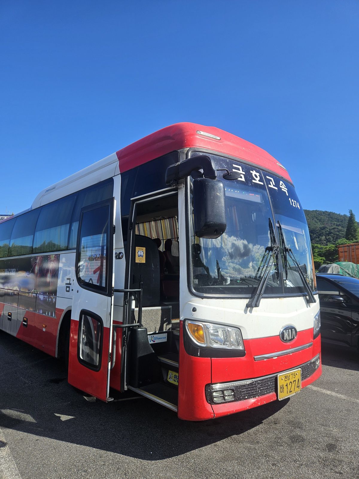 Un bus KIA rouge et blanc stationné sous un ciel bleu dégagé.