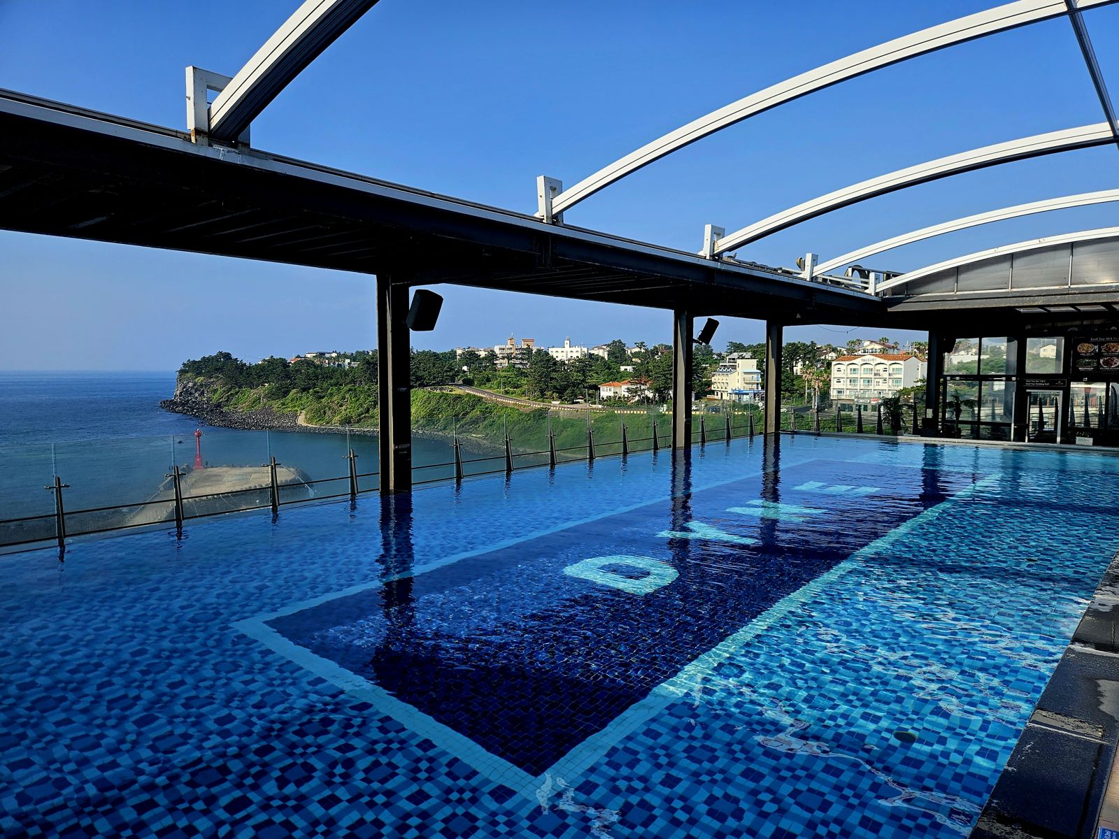 Vue de la piscine à débordement de l'hôtel, avec la mer en arrière-plan et le ciel bleu.