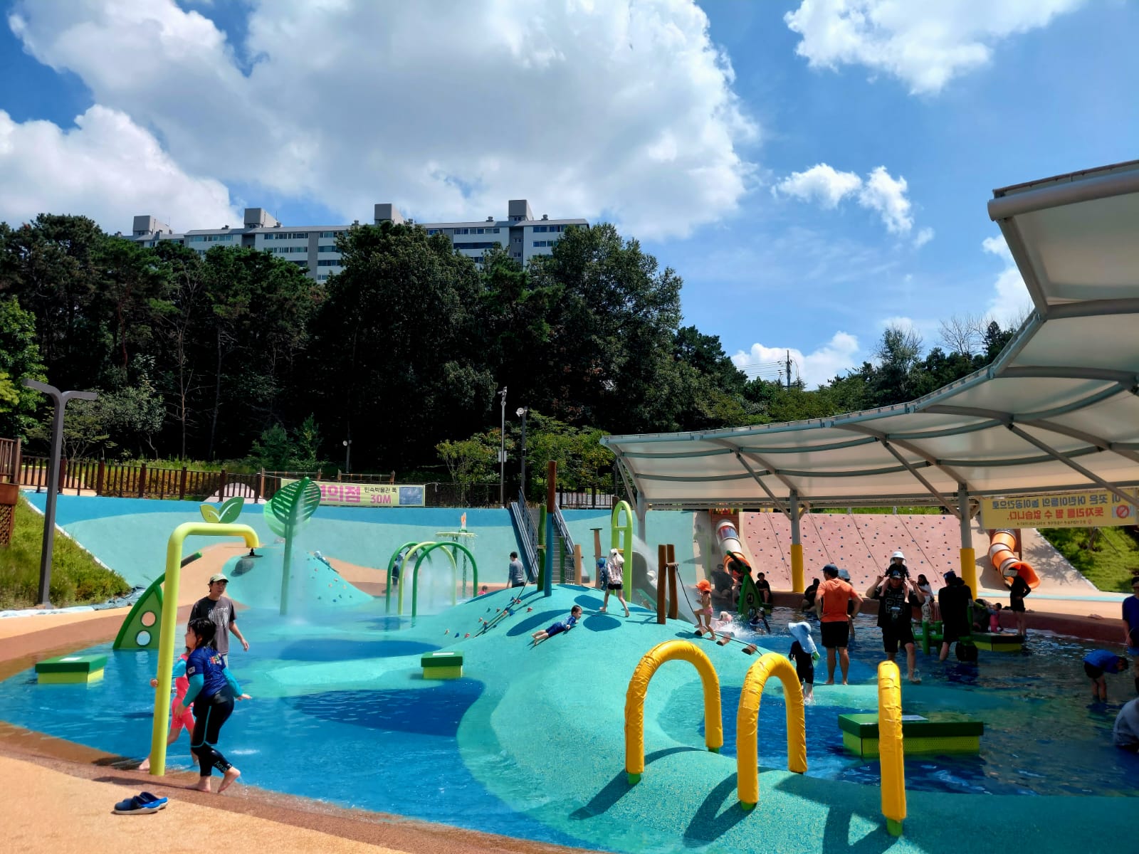 Un parc aquatique pour enfants avec des jeux d'eau et des toboggans, entouré d'une verdure luxuriante sous un ciel bleu.