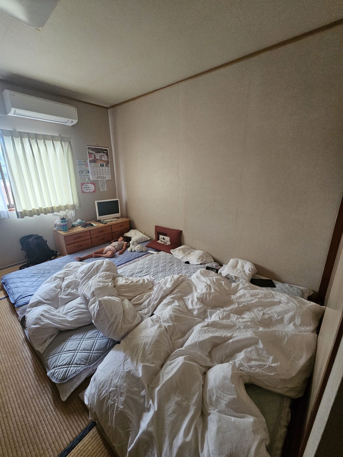 Chambre d'hôtel japonaise avec deux matelas et des couvertures en désordre, une petite télévision et une fenêtre laissant entrer la lumière.