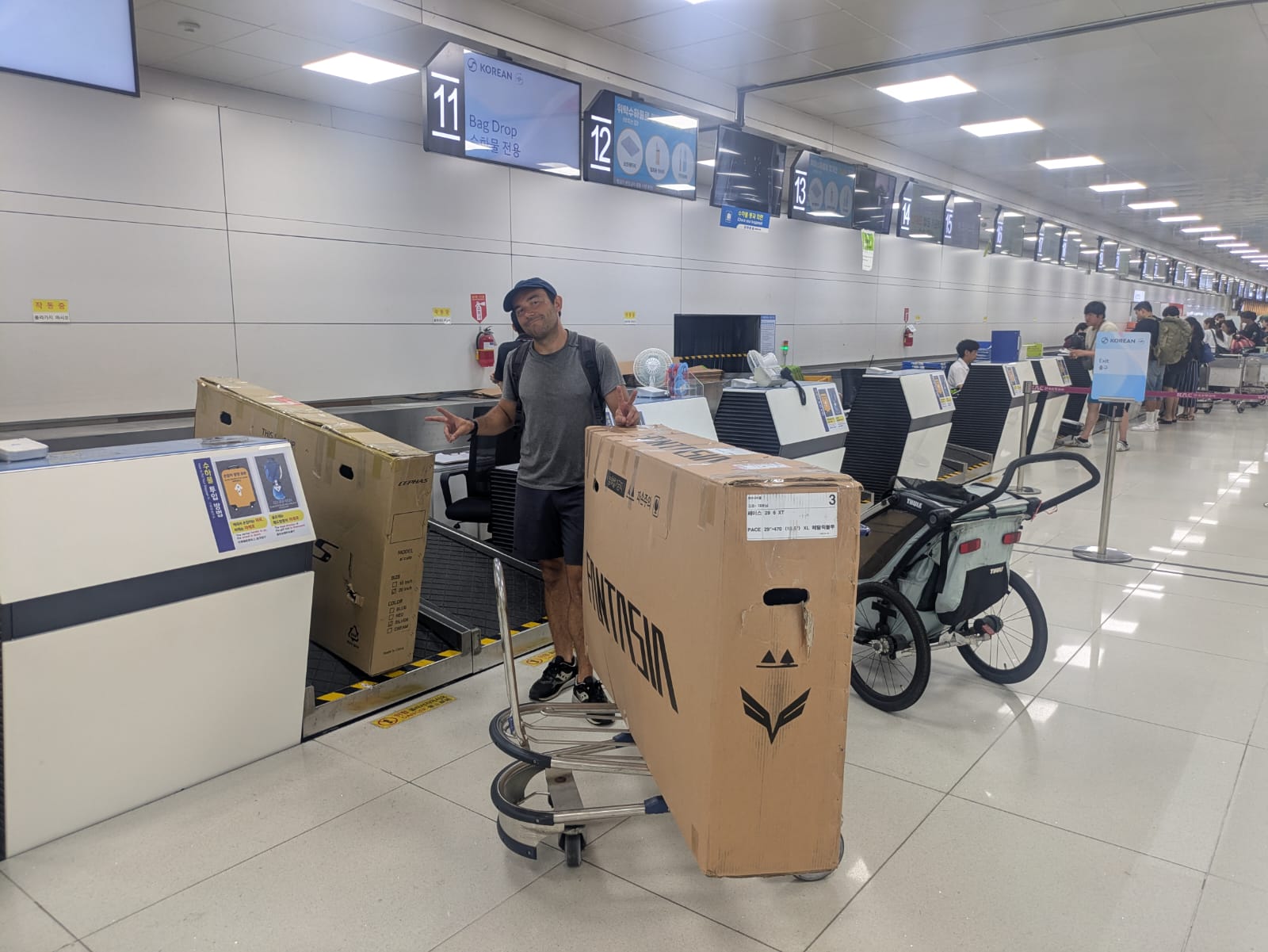 Un homme debout à un comptoir d'enregistrement d'aéroport, posant avec deux grands cartons de vélo prêts à être enregistrés.