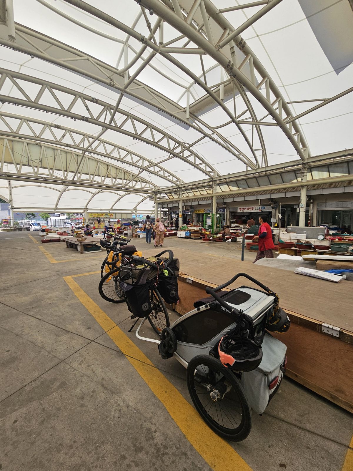 Des vélos stationnés sous une structure couverte, avec des étals de marché visibles en arrière-plan.