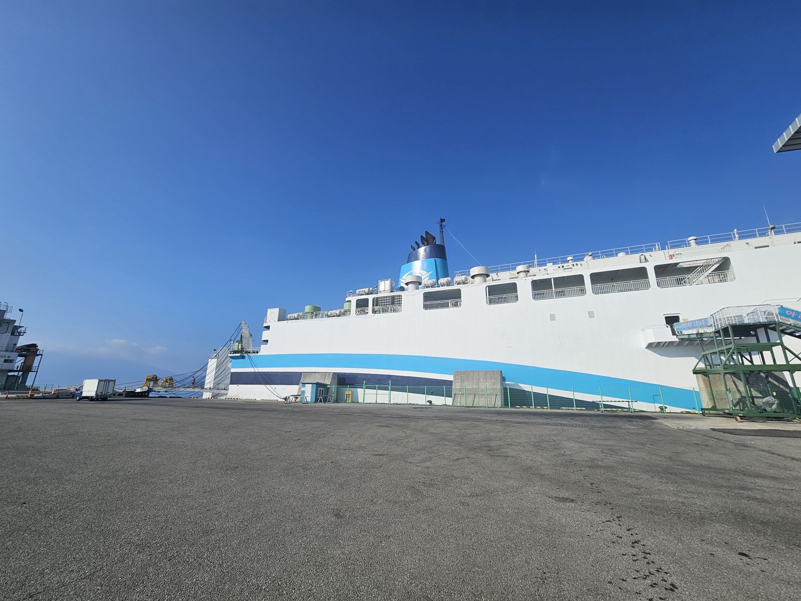 Un immense ferry amarré au port sous un ciel bleu, avec une rampe d'accès visible et un quai en béton.