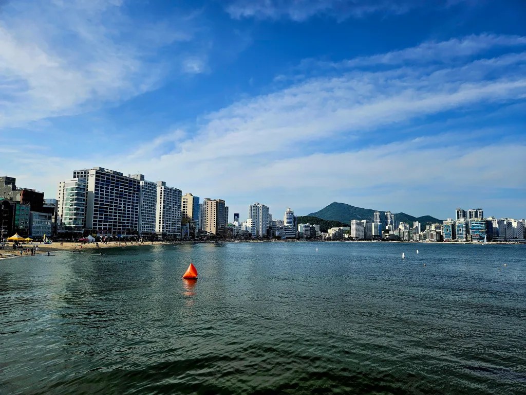 Vue de la plage de Busan avec des gratte-ciels en arrière-plan et un drapeau orange flottant sur l'eau.