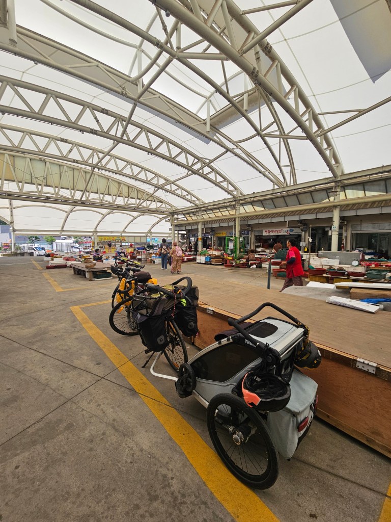 Des vélos stationnés sous une structure couverte, avec des étals de marché visibles en arrière-plan.