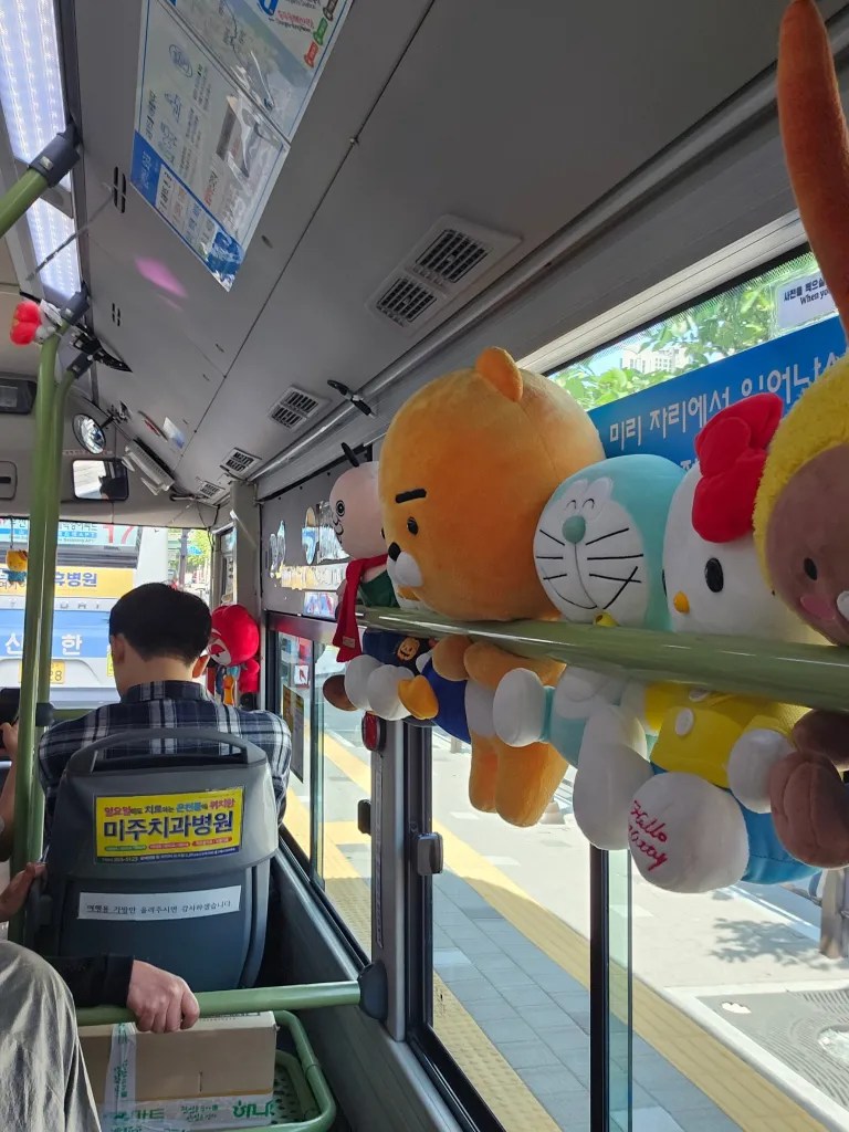 Intérieur d'un bus en Corée du Sud, avec des peluches colorées accrochées aux barres de maintien et un passager assis à l'avant, regardant à l'extérieur.