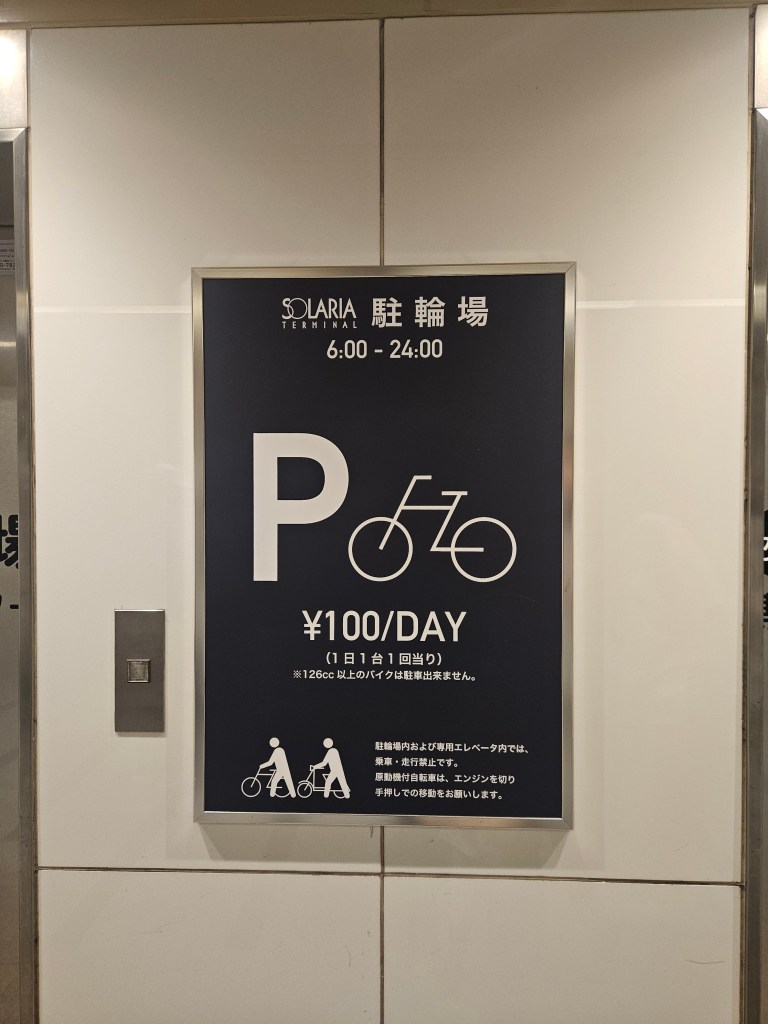 Panneau indiquant un parking à vélos à Solaria Terminal, avec les heures d'ouverture et le tarif journalier de 100 yens.