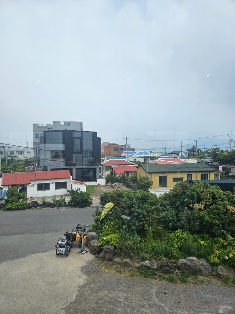 Vue d'un quartier de Seogwipo avec des bâtiments modernes et traditionnels, des maisons aux toits colorés, et des vélos stationnés sur le côté.