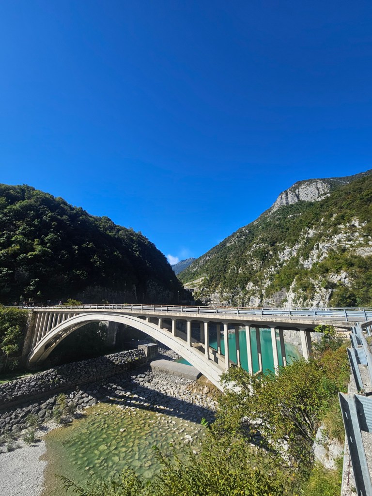 Un pont en béton élégant surplombe une rivière calme, entouré de collines verdoyantes sous un ciel bleu clair.
