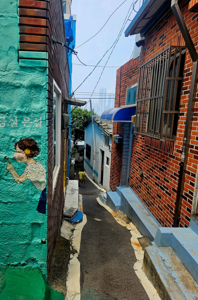 Une ruelle pittoresque à Huinnyeoul avec des maisons colorées, une fresque murale représentant une petite fille et un chemin pavé menant à des bâtiments historiques.