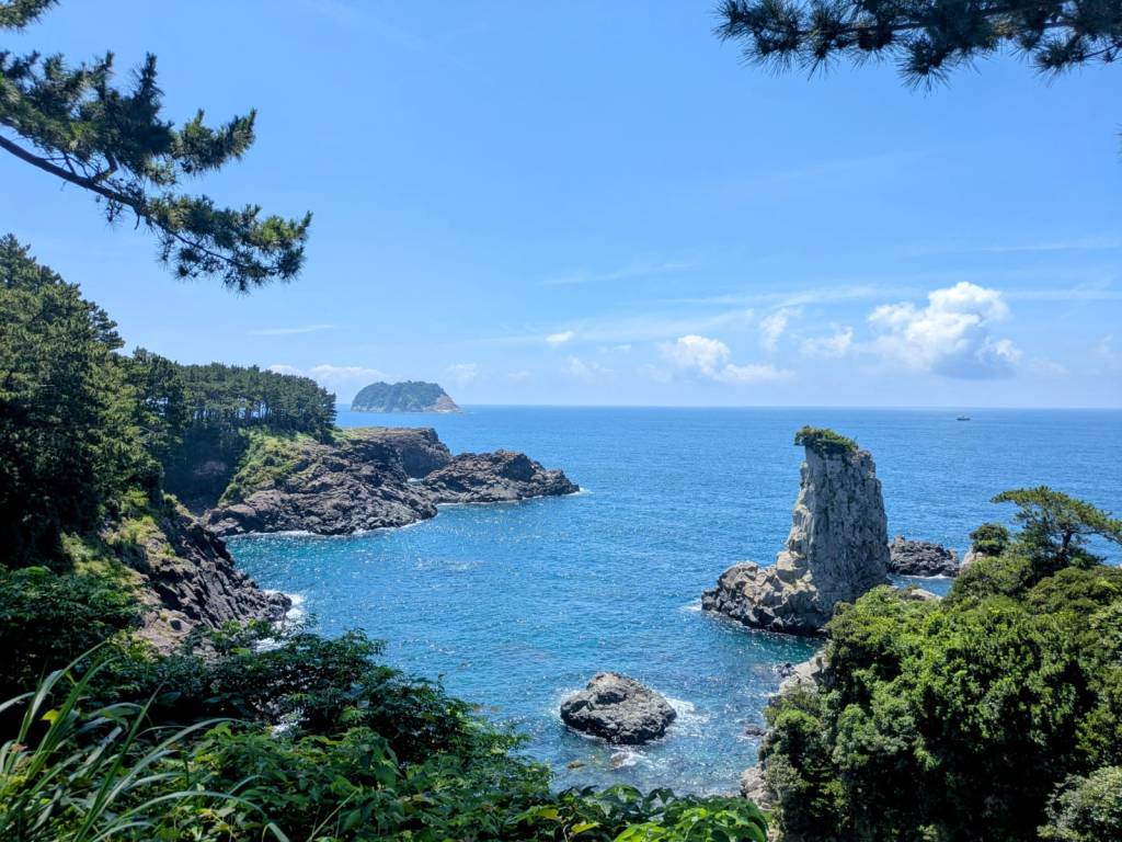 Vue côtière sur l'île de Jeju, avec rochers émergeants de l'eau turquoise et végétation verdoyante.
