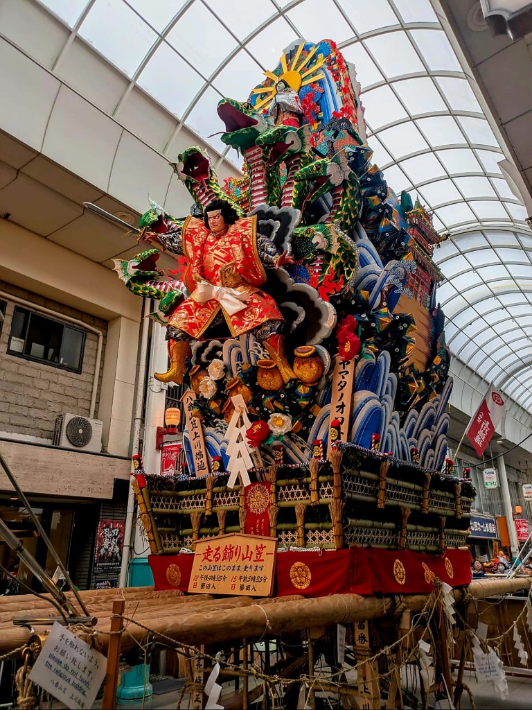 Un char coloré exposé dans une rue de Fukuoka, décoré avec des figures traditionnelles et des motifs de dragons, représentant le festival Hakata Gion Yamakasa.