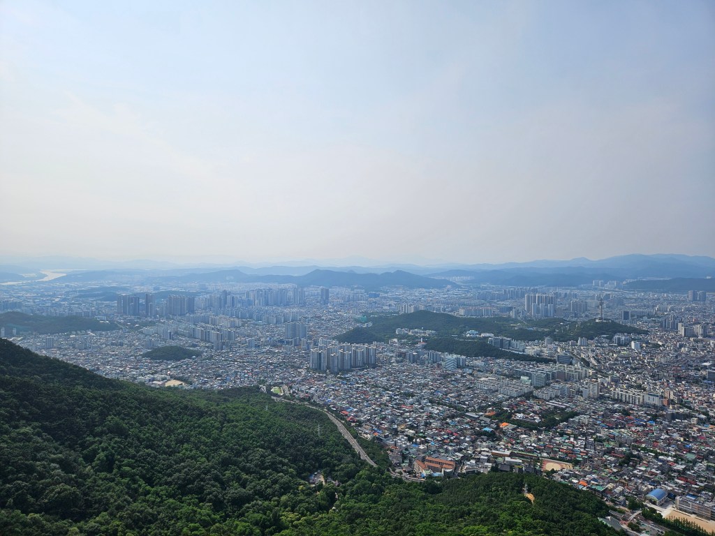 Vue panoramique de la ville de Daegu, en Corée du Sud, depuis le sommet de la montagne d'Apsan, montrant un mélange de développement urbain et de verdure environnante.
