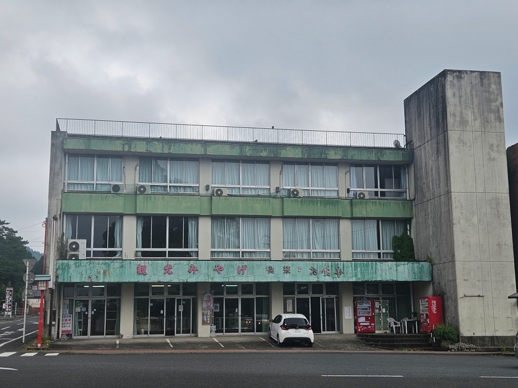 Vue d'un hôtel ancien et décrépit à Kirishima, Japon, avec un extérieur en métal vert et des fenêtres blanches.