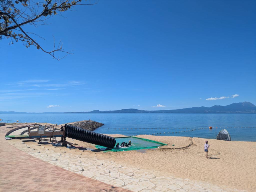 Vue d'une plage avec du sable doré et une mer calme, un enfant jouant près d'une structure de jeux en bois.