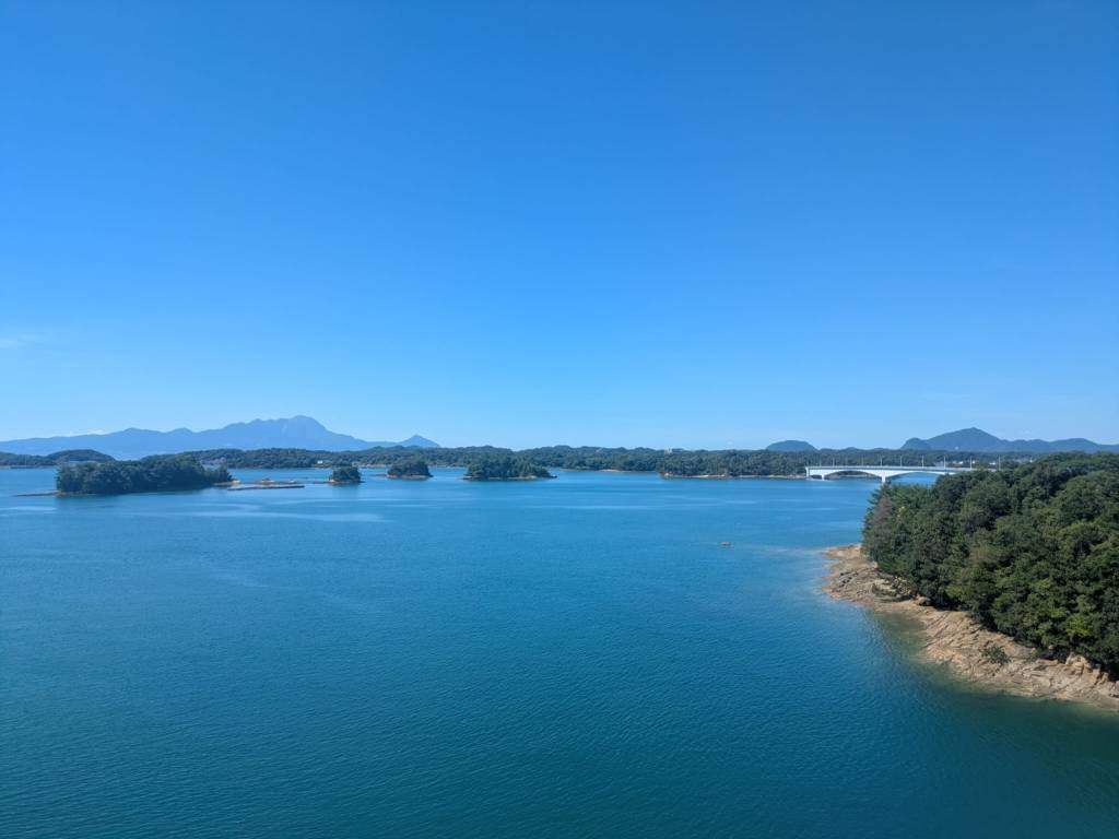 Vue panoramique d'une baie avec des îles dispersées, entourée de montagnes sous un ciel bleu clair.