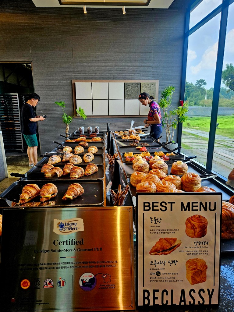 Buffet de pâtisseries comprenant des croissants et autres douceurs, avec un panneau présentant le meilleur menu dans un café moderne en Corée du Sud.