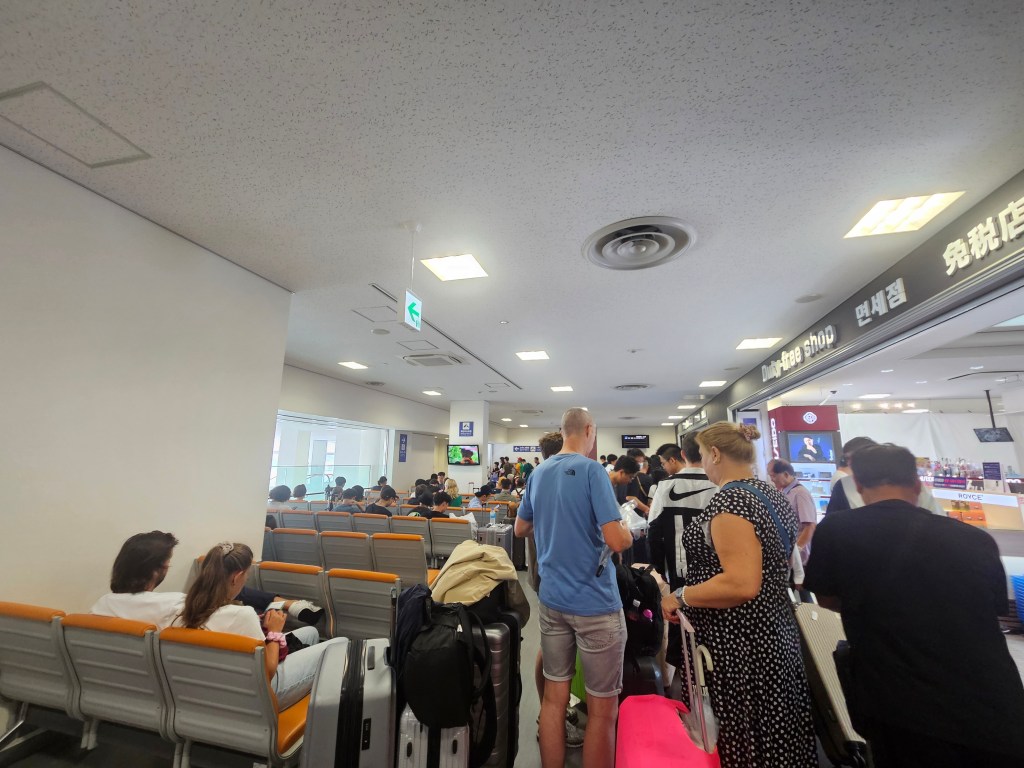 Une foule de passagers attendant à l'enregistrement dans un terminal de ferry, avec des bagages et des sièges vides en arrière-plan.