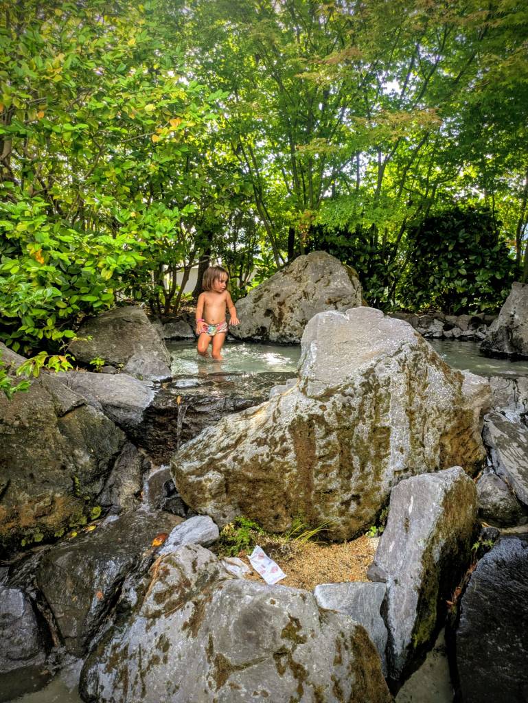 Un enfant joue dans un petit bain d'eau entouré de rochers et de verdure.