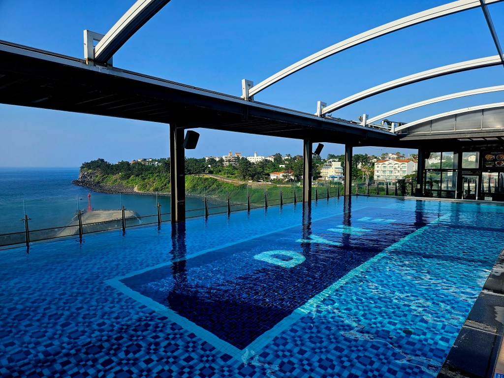 Vue de la piscine à débordement de l'hôtel, avec la mer en arrière-plan et le ciel bleu.